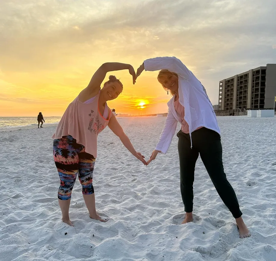 Two friends making a heart shape on the beach at sunset